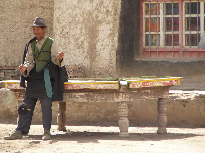 Tibetan man spinning wool while leaning against an outdoor pool table. Shigatse, Tibet.